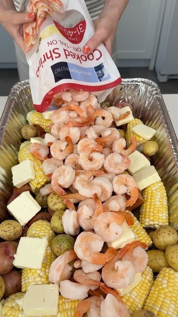 shrimp, corn on the cob, potatoes and cheese are being poured into a baking dish