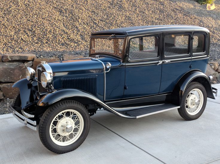 an old blue car parked in front of a stone wall