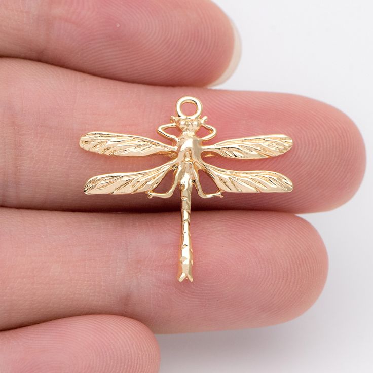 a small gold dragonfly charm on someone's finger