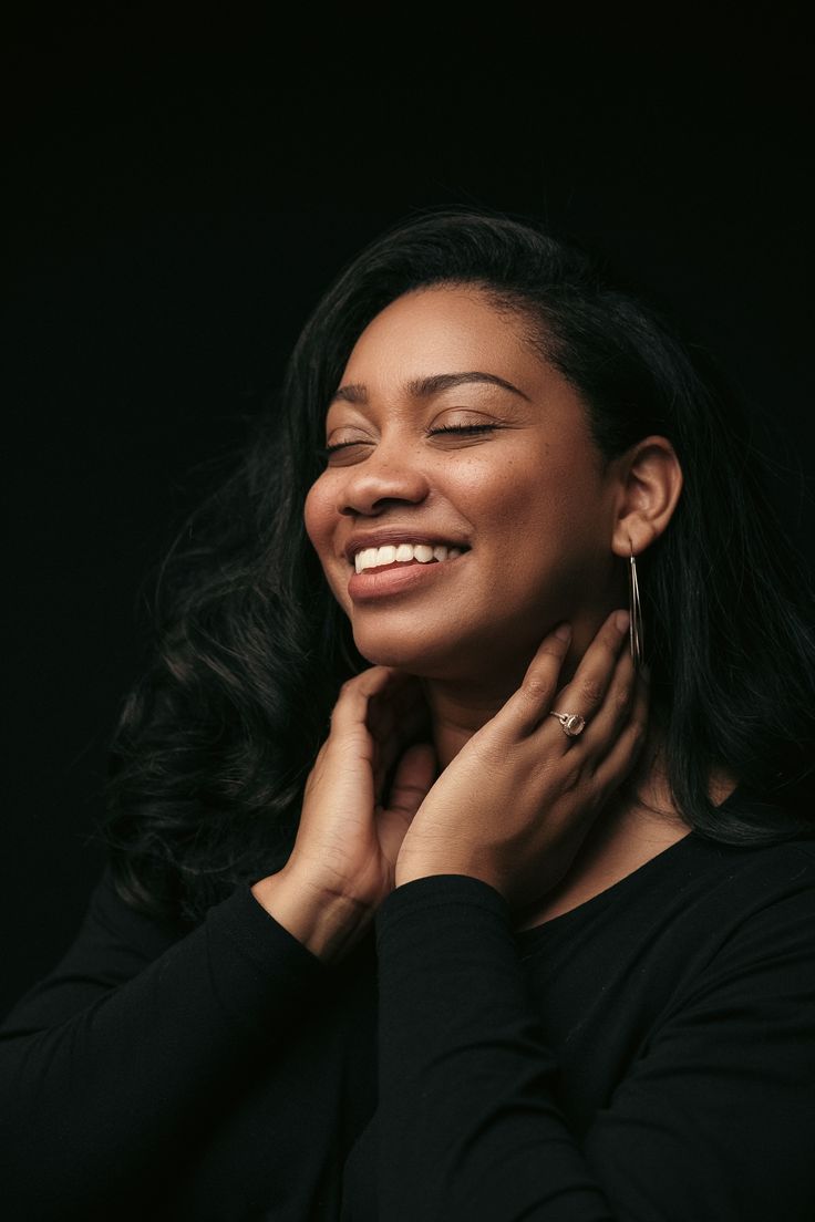 a woman smiling with her hands on her chest and holding her neck in front of her face