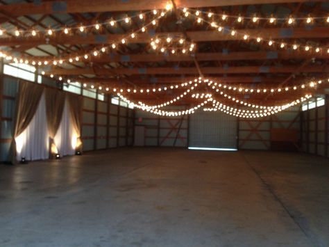 an empty barn with lights strung from the ceiling