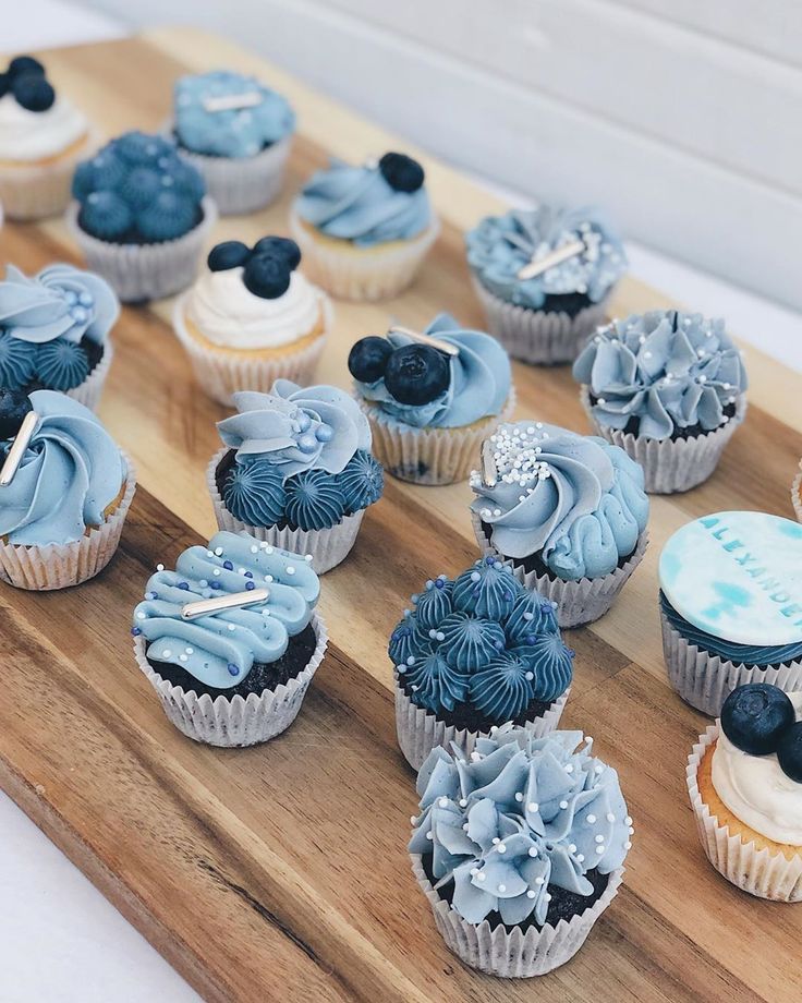 cupcakes with blue frosting are arranged on a wooden tray