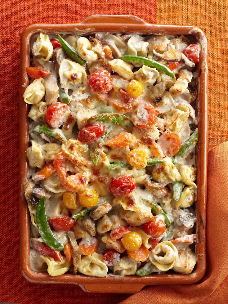 a casserole dish filled with pasta, tomatoes and green beans on a red cloth