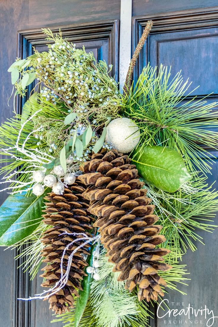 a wreath with pine cones and greenery is hanging on the front door