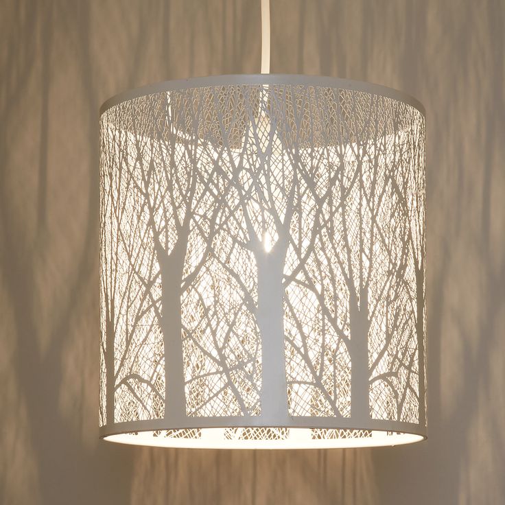 a white lamp hanging from a ceiling with trees on it's side and the light shining through