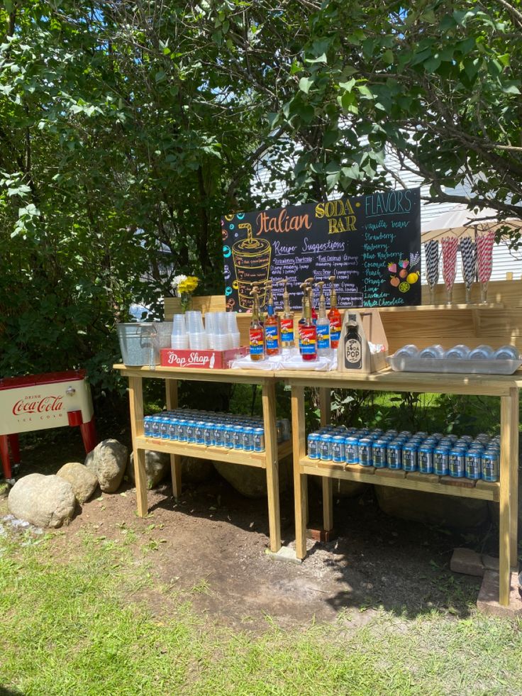 a wooden table topped with lots of bottles and glasses next to a chalkboard sign