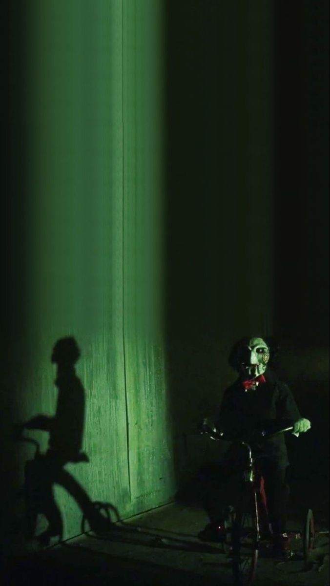 the shadow of a person on a bike in front of a green wall with light coming from it