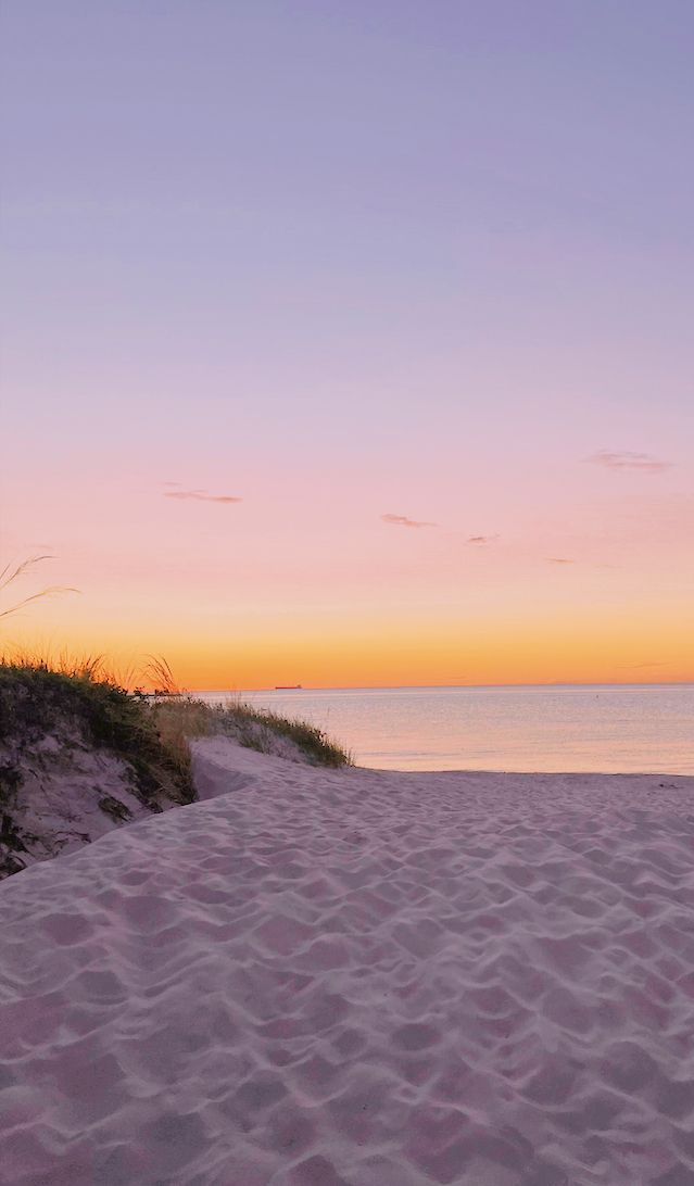 the sun is setting at the beach and there are sand dunes in front of the water