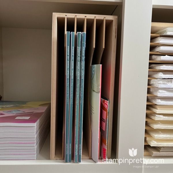 a book shelf filled with lots of books on top of a white counter next to a stack of folders