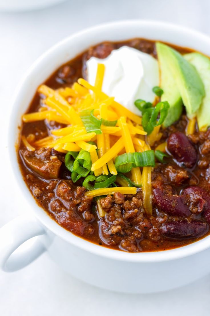 a white bowl filled with chili, cheese and avocado on top of a table