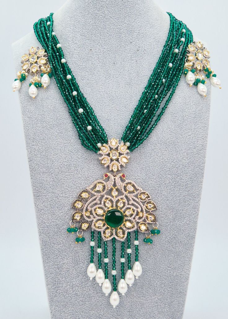 "Tyaani Kundan Double Peacock Mala Necklace/Emerald Green Long Necklace Set/Indian Jewelry/Rani Haar/Bridal Necklace Set/Pakistani Jewelry Enhance your special event with the mesmerizing Emerald Green necklace set that showcases Kundan embellishments and a mala made of hydro beads. Make sure to grab this exquisite jewelry piece before it's too late! Necklace Length: 16\" Neckline has an adjustable doori. Earring Lenght: 2\" Push-Back closure Weight : 12 gms each. Dual-tone finish on high-quality brass as a base metal. Availability: In-Stock. *Color may vary slightly due to light condition & photography. Jewelry Care:  Keep away from moisture. Allow perfumes and lotion to dry before wearing. Store in jewelry pouch. Clean only with soft lint-free cloth.  At Sparkling Trendz, we offer a wide Festive Hand Set Emerald Necklace, Wedding Kundan Necklace With Emerald Intricate Design, Traditional Green Emerald Necklace, Green Bollywood Necklace With Peacock Design, Green Kundan Emerald Necklace With Intricate Design, Green Bollywood Necklaces With Peacock Design, Green Necklace With Peacock Design For Diwali, Emerald Kundan Necklace For Wedding And Festivals, Green Peacock Design Necklace For Diwali