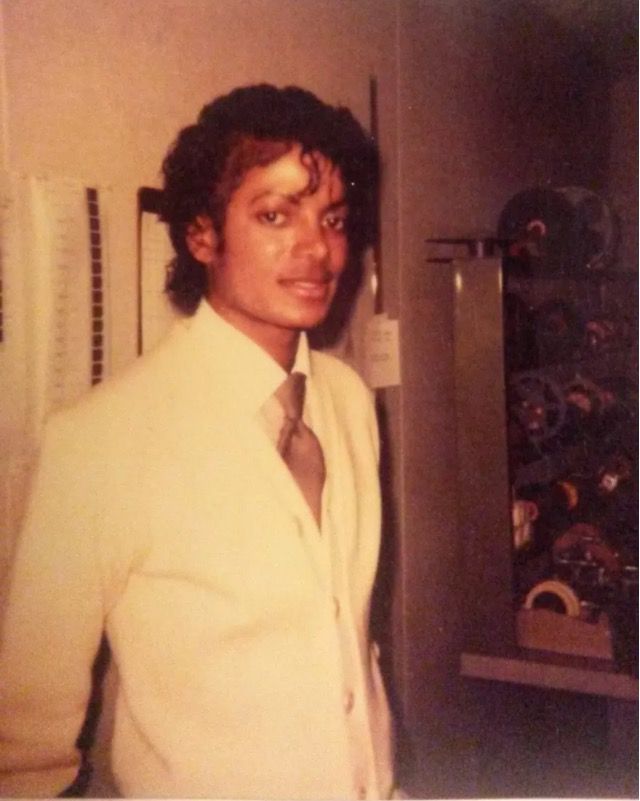 a man in a white suit and tie standing next to a wall filled with magnets