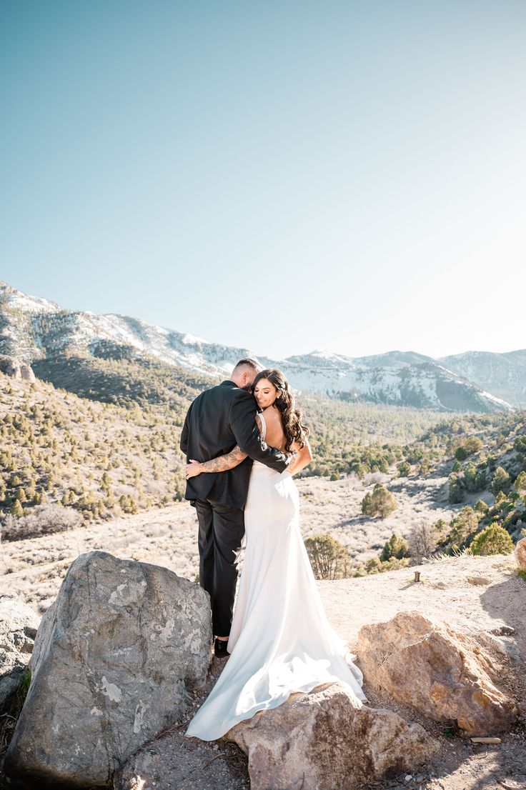 Capturing pure romance as the bride embraces her groom atop a scenic rock at Mount Charleston. Her timeless wedding dress cascades elegantly, paired perfectly with his classic black suit. 🌟 Venture into unique wedding ideas with this stunning wildflower wedding theme in the crisp mountain air. Dream-worthy wedding goals! 💖 #weddingdresses #weddingideas #mountainwedding #wildflowerweddingtheme #timelessweddingdress Classic Black Suit, Wildflower Wedding Theme, Timeless Wedding Dress, Unique Wedding Ideas, Las Vegas Wedding, Pure Romance, Wildflower Wedding, Las Vegas Strip, Wedding Goals