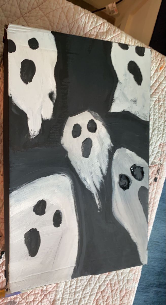 a painting with black and white ghost faces painted on it's canvases in front of a bed