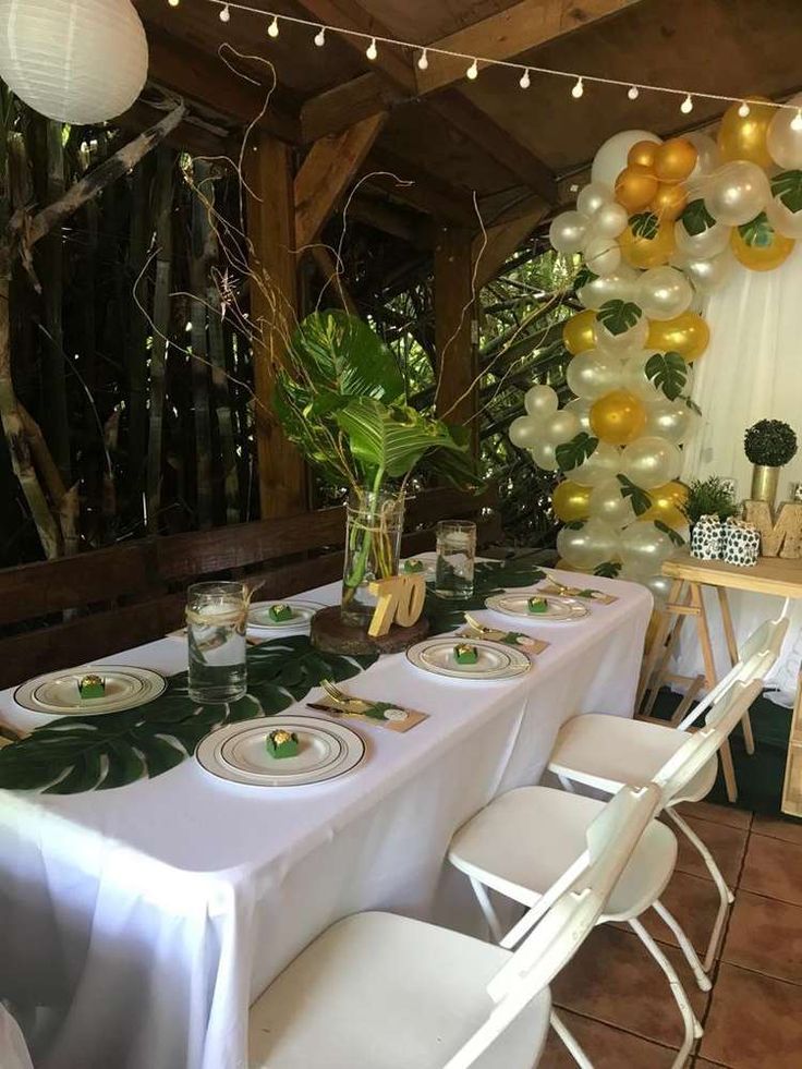 a table set up for a party with balloons and greenery