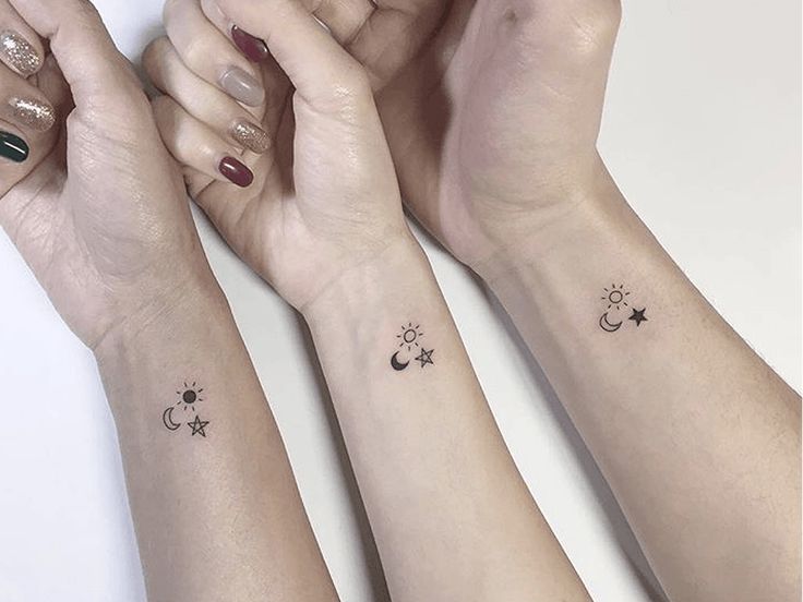 three girls with matching tattoos on their arms holding hands and looking at each other's wrist