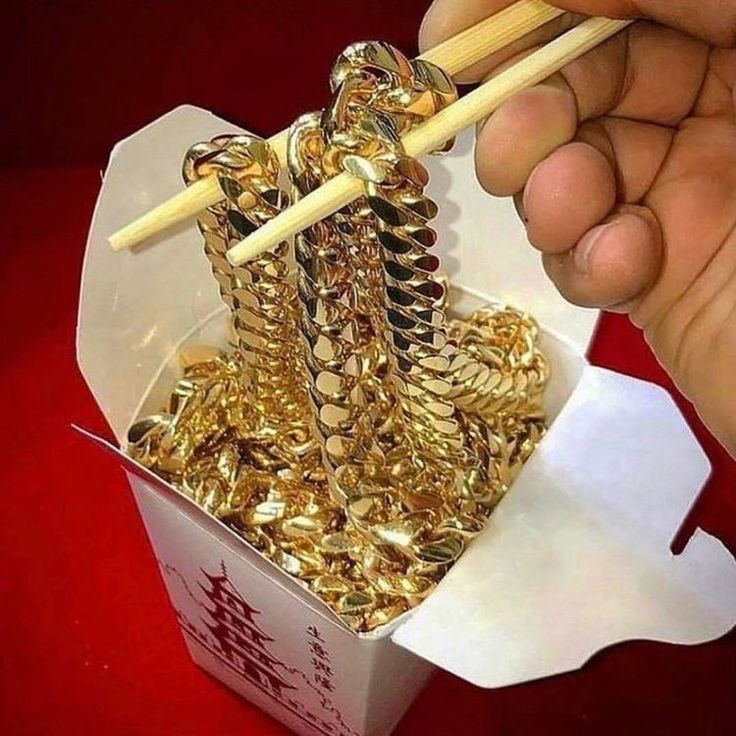 a person holding chopsticks over a box filled with gold coins