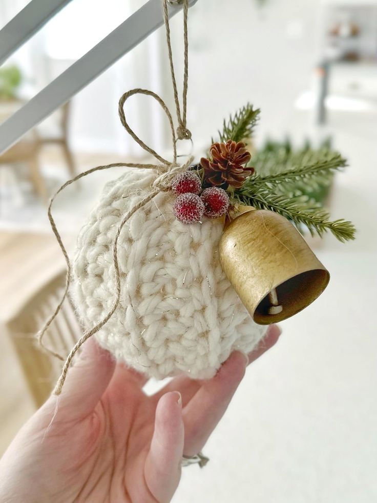 a hand holding a christmas ornament with a bell and pine cone on it