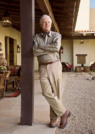 an older man leaning on the side of a building with his arms crossed and looking at the camera