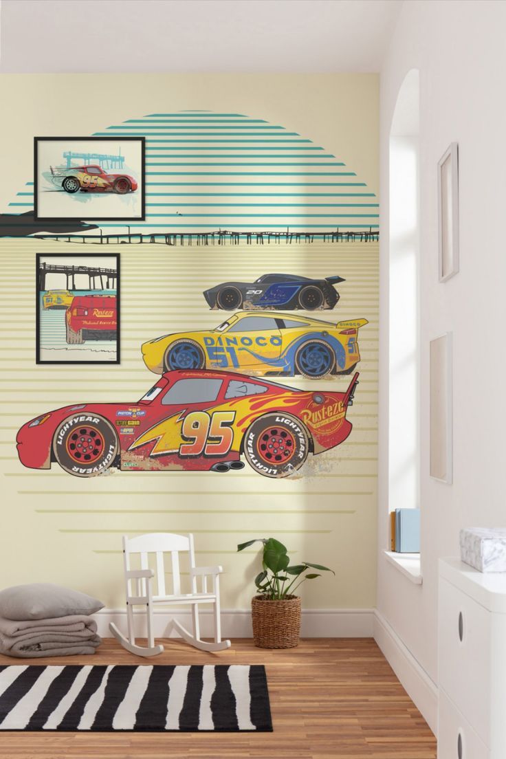 a room with a rug, chair and wall mural depicting cars on the track in front of a window