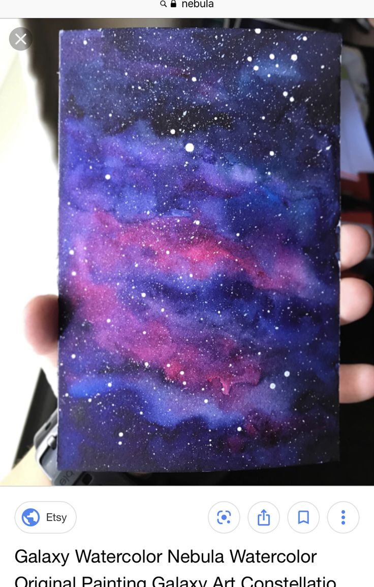 a hand holding up a piece of paper with watercolor paint on it and stars in the sky