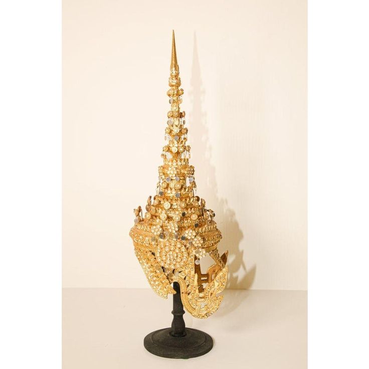 Ceremonial Thai headdress usually worn for wedding or religious ceremonies. Hand-crafted in Thailand. Gilt Thai Ceremonial Headdress circa 20th century. A traditionally modeled design with a conical metal spire at the top, in gilt papier mâché, metal and glass gemstones displayed on a black wooden stand. Dimensions: H 26 in. x W 11 in. x D 9 in. Gold Ceremonial Headpiece With Tall Crown, Traditional Gold Headpiece With Structured Crown, Traditional Gold Structured Crown Headpiece, Traditional Gold Crown Headpiece, Traditional Gold Headpiece With Tall Crown, Traditional Gold Ceremonial Headpieces, Ceremonial Tall Crown Headpiece For Festivals, Religious Ceremony, Head Dress