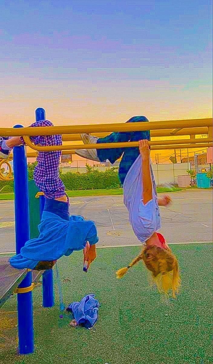 two children are playing on a playground with their hands in the air and one child is upside down