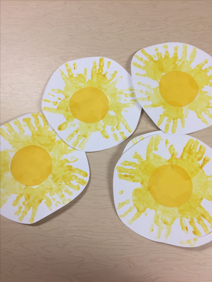 three paper plates with yellow handprinted eggs sitting on top of a wooden table