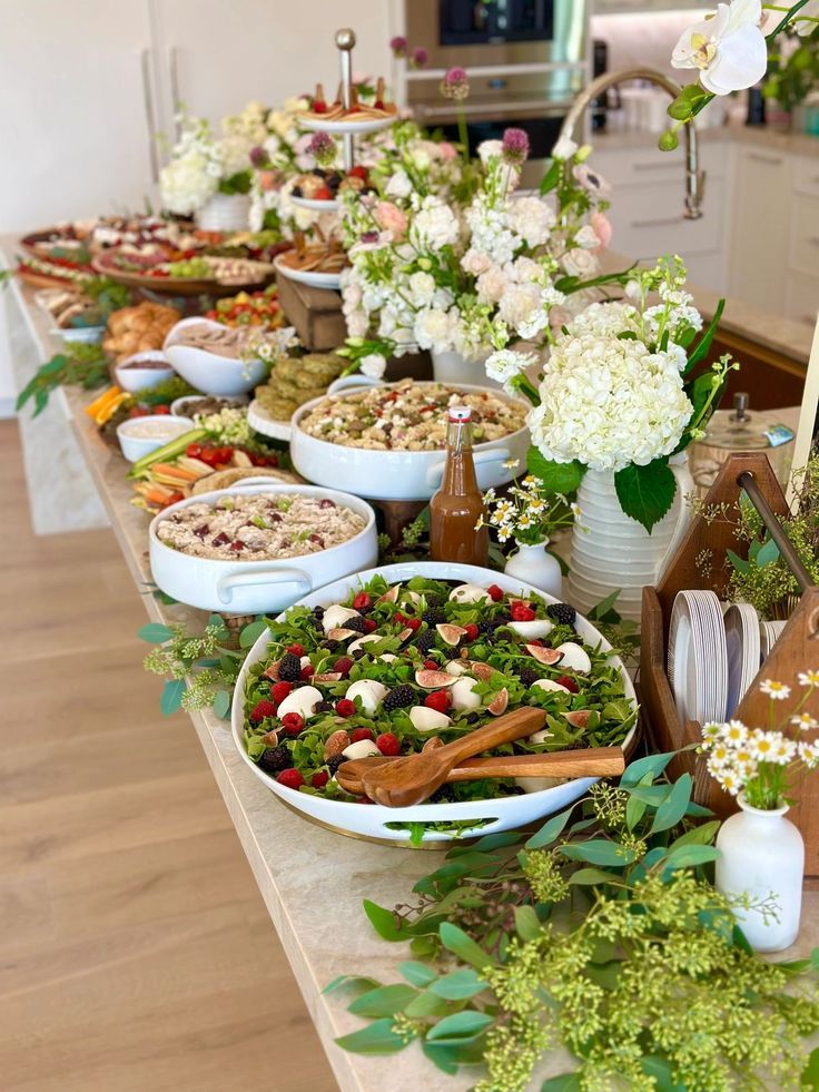 a table filled with lots of food and flowers on it's sides, including salads