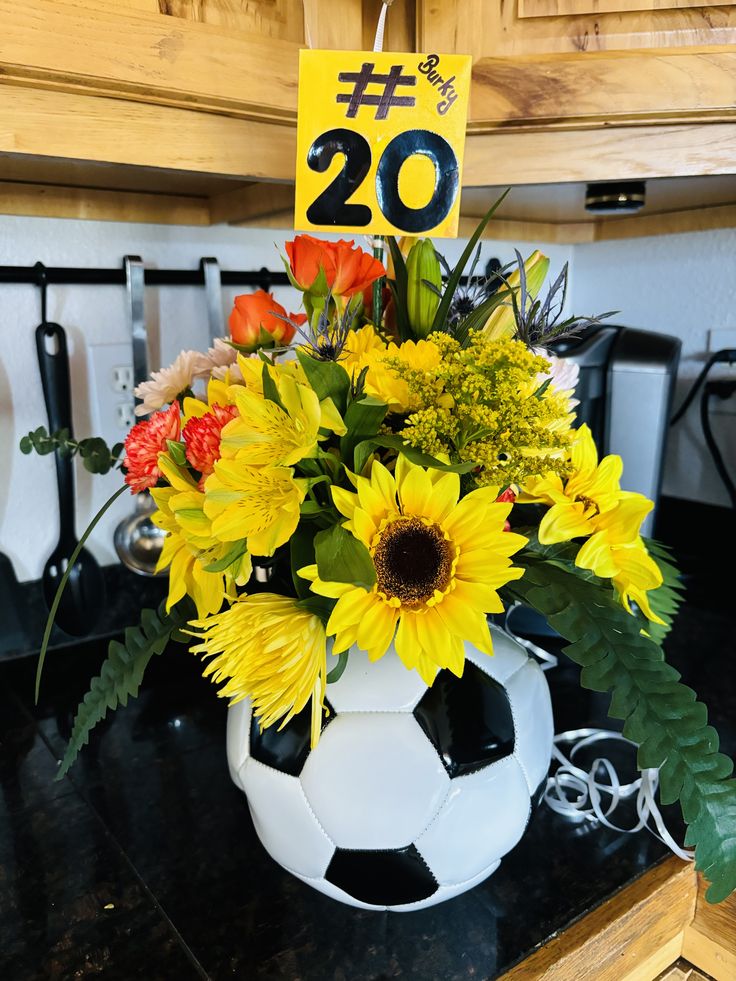 a soccer ball with flowers in it sitting on a counter next to a sign that reads 20