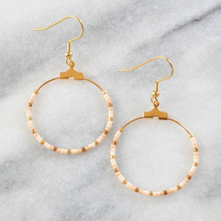 Your soon-to-be favorites, these small gold beaded hoops (available in 22 exclusive patterns) are perfect for day, night and well, everything in between. gold-plated hoop and hooks lead-free and nickel-free glass seed beads plastic earring back 1.25" in diameter and overall length is 2" from top of hook packaged on a hand-stamped kraft earring card in a clear resealing bag EXCLUSIVE STYLES NAVY Navy blue, bronze, and blush PHOENIX Turquoise, red, cream, and gold GREY Matte black, metallic pink, Gold Heishi Beads Earrings, Gold Heishi Beaded Earrings With Colorful Beads, Gold Heishi Bead Earrings With Colorful Beads, Gold Dangling Heishi Beads Earrings, Gold Hoop Earrings With Tiny Beads For Summer, Adjustable Hoop Earrings With Gold Beads As Gift, Adjustable Gold Beads Hoop Earrings As Gift, Adjustable Gold Beaded Hoop Earrings As Gift, Summer Tiny Beads Small Hoop Earrings