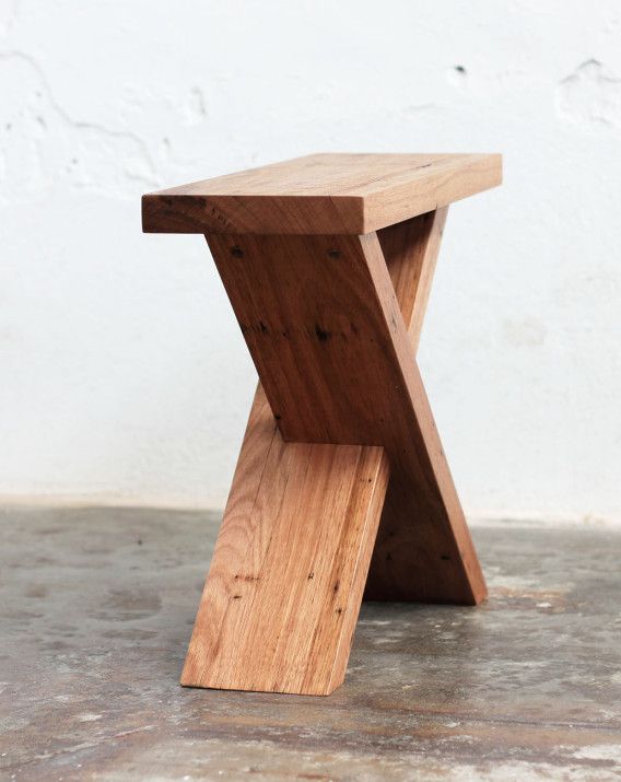 a small wooden bench sitting on top of a cement floor next to a white wall