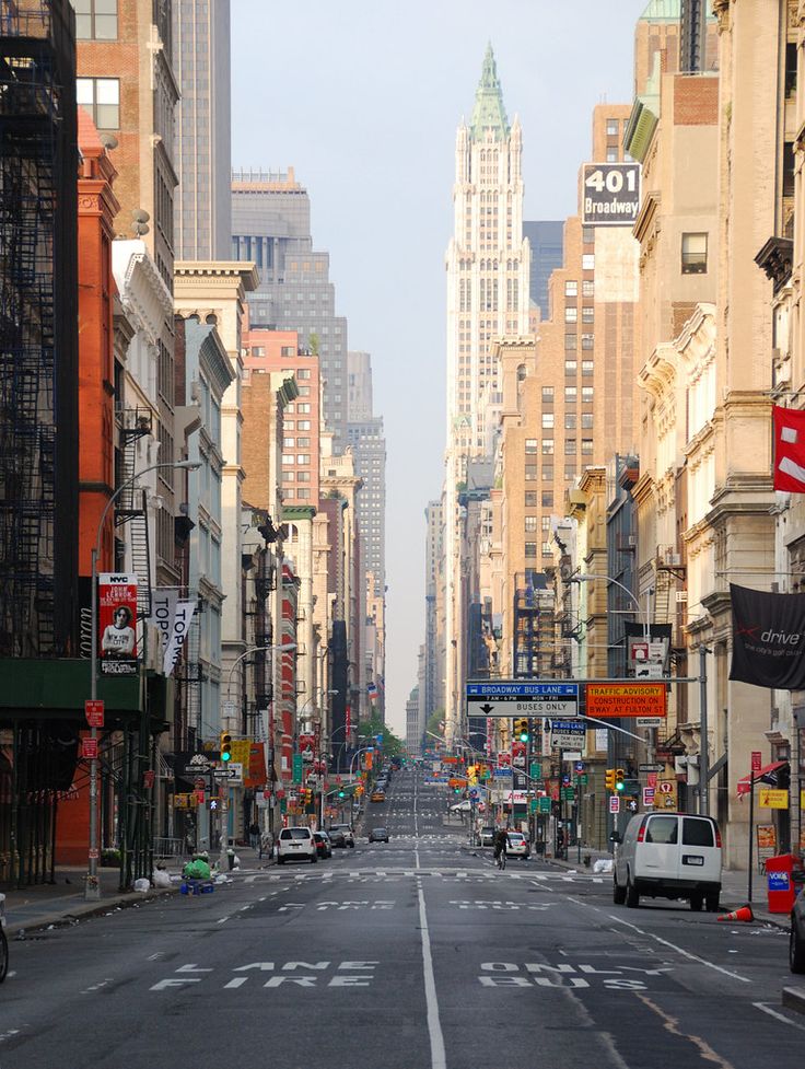 an empty city street with tall buildings on both sides and cars driving down the road