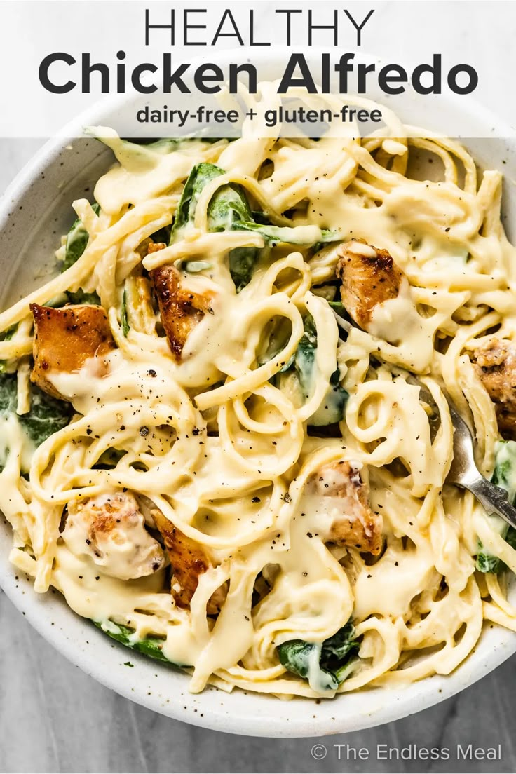 a white bowl filled with pasta covered in chicken and spinach sauce on top of a marble table