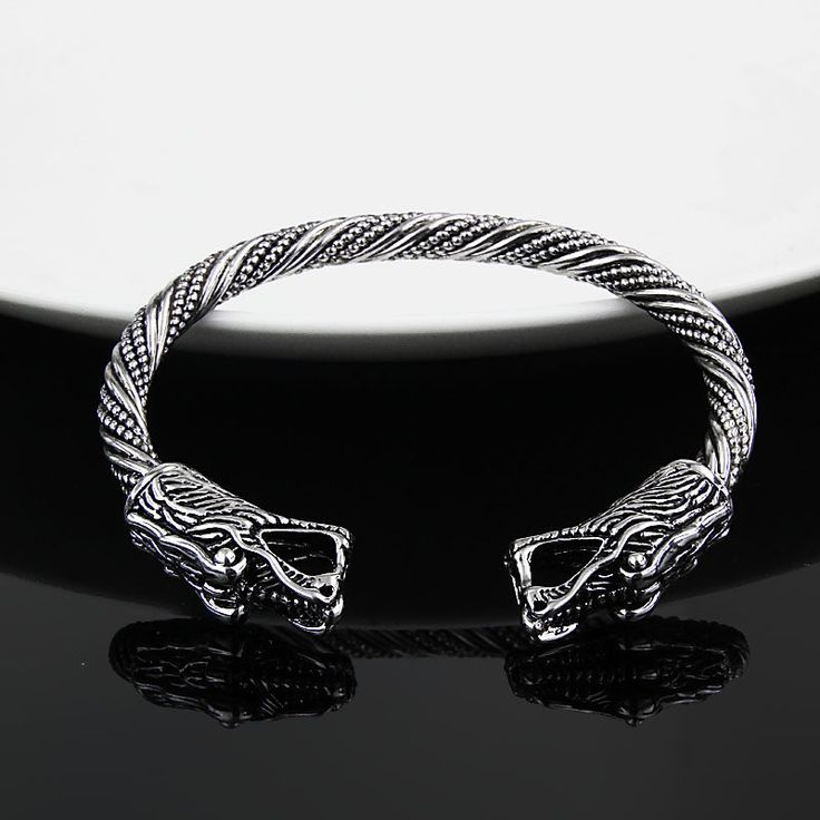 a silver bracelet with an intricate design on the front and back ends, sitting on a black surface