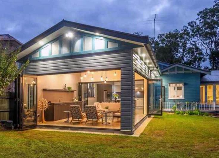 a small house is lit up at night with lights on the windows and patio furniture