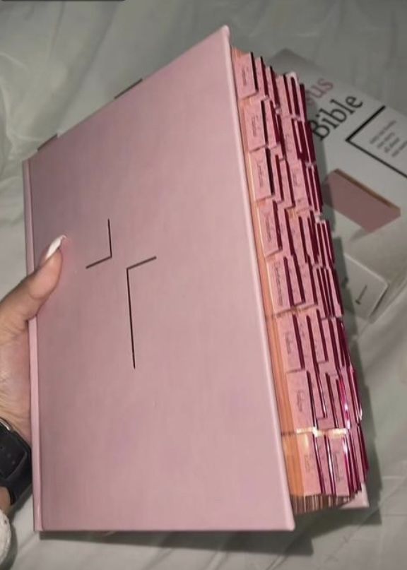 a person holding a pink box with a cross on the front and side, in their left hand