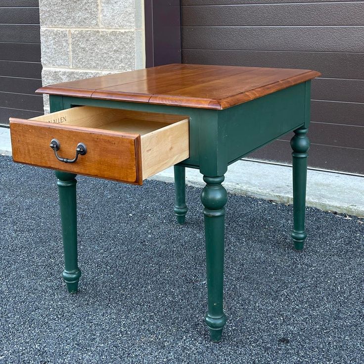 a green table with a drawer on it sitting in front of a garage door next to a brick wall