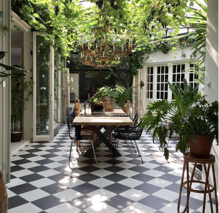 an outdoor dining area with black and white checkered tile flooring, potted plants on the table