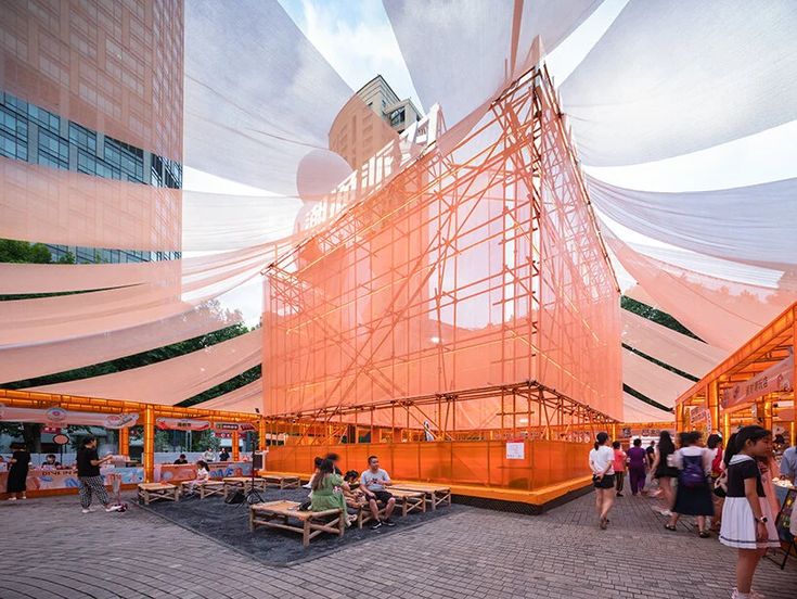 people are gathered around an orange structure with scaffolding on it's sides