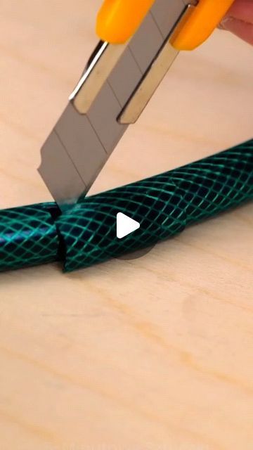 a person using a pair of scissors to cut a piece of green wire on a wooden surface