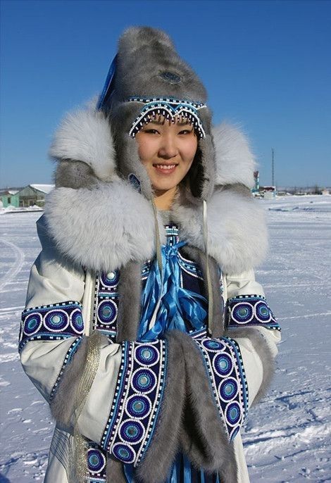 a woman wearing a fur hat and scarf in the snow with her hands on her hips