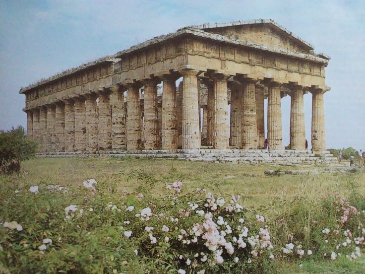 an old building with many columns and flowers in the foreground