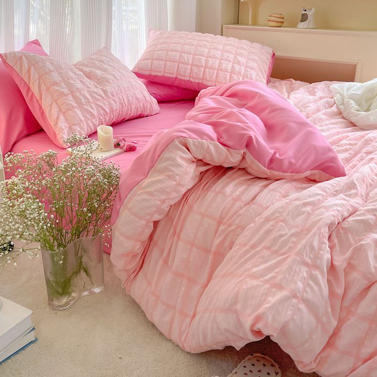 a bed with pink comforters and pillows in a bedroom next to a vase filled with baby's breath flowers