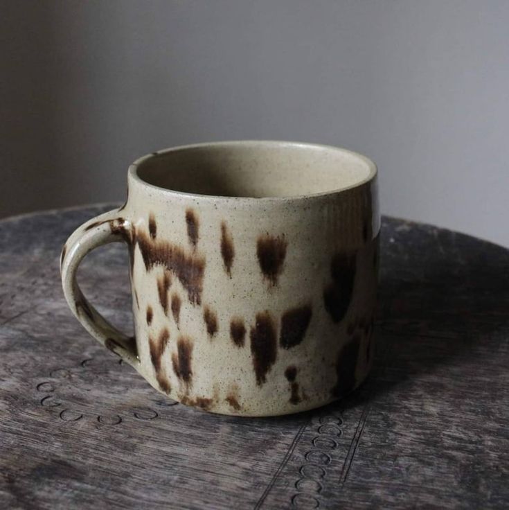 a white and brown cup sitting on top of a wooden table next to a wall