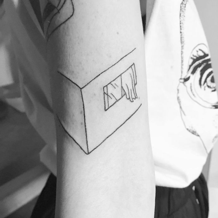 a black and white photo of a woman's arm with a small house tattoo on it