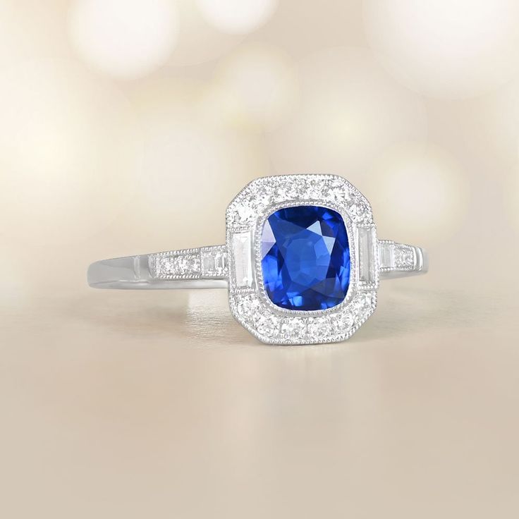 This item has just been reserved by another customer. Please contact us to be notified if it becomes available.  This milgrain bezel set ring is adorned with a cushion cut sapphire weighing 1.06 carats, which is held securely in place by a bezel setting. Encircling the central sapphire is a halo of round brilliant cut diamonds that accentuates its beauty, and on either side, two baguette cut diamonds add an extra touch of elegance.  The total diamond weight of this milgrain bezel set ring is app Cushion Cut Sapphire Ring, Estate Diamond Jewelry, Rare Jewelry, Bezel Set Ring, Halo Earrings, Baguette Cut Diamond, Set Ring, Platinum Ring, Baguette Cut