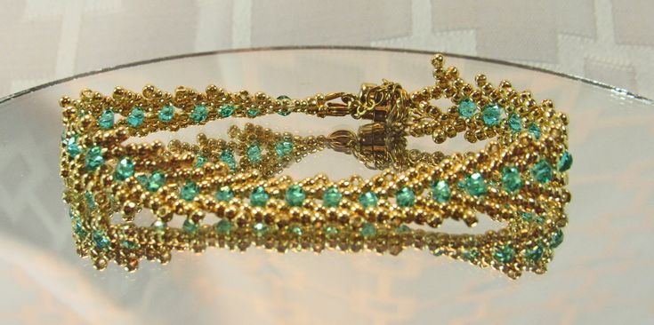 a gold and green beaded bracelet sitting on top of a glass table