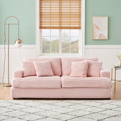 a pink couch sitting in front of a window next to a white rug and lamp