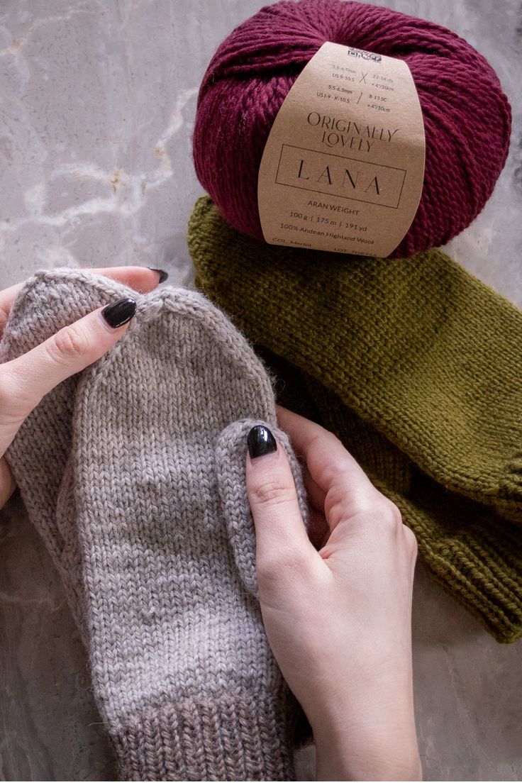 a woman is holding two balls of yarn next to her mitts and one ball of yarn